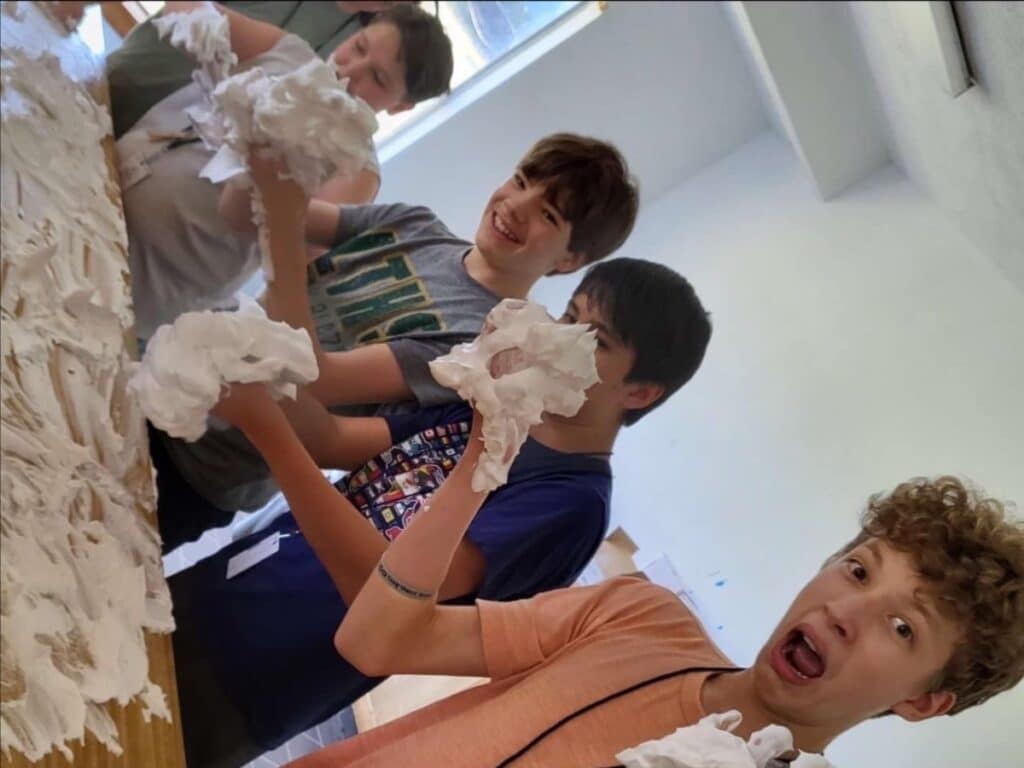 Four campers laughing while experimenting with shaving cream on a table.