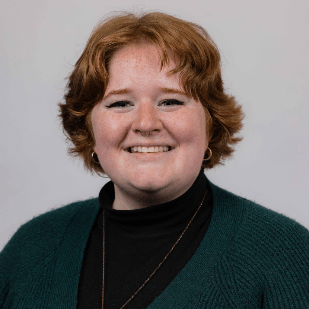 Head shot of Brooke smiling in front of solid gray background.